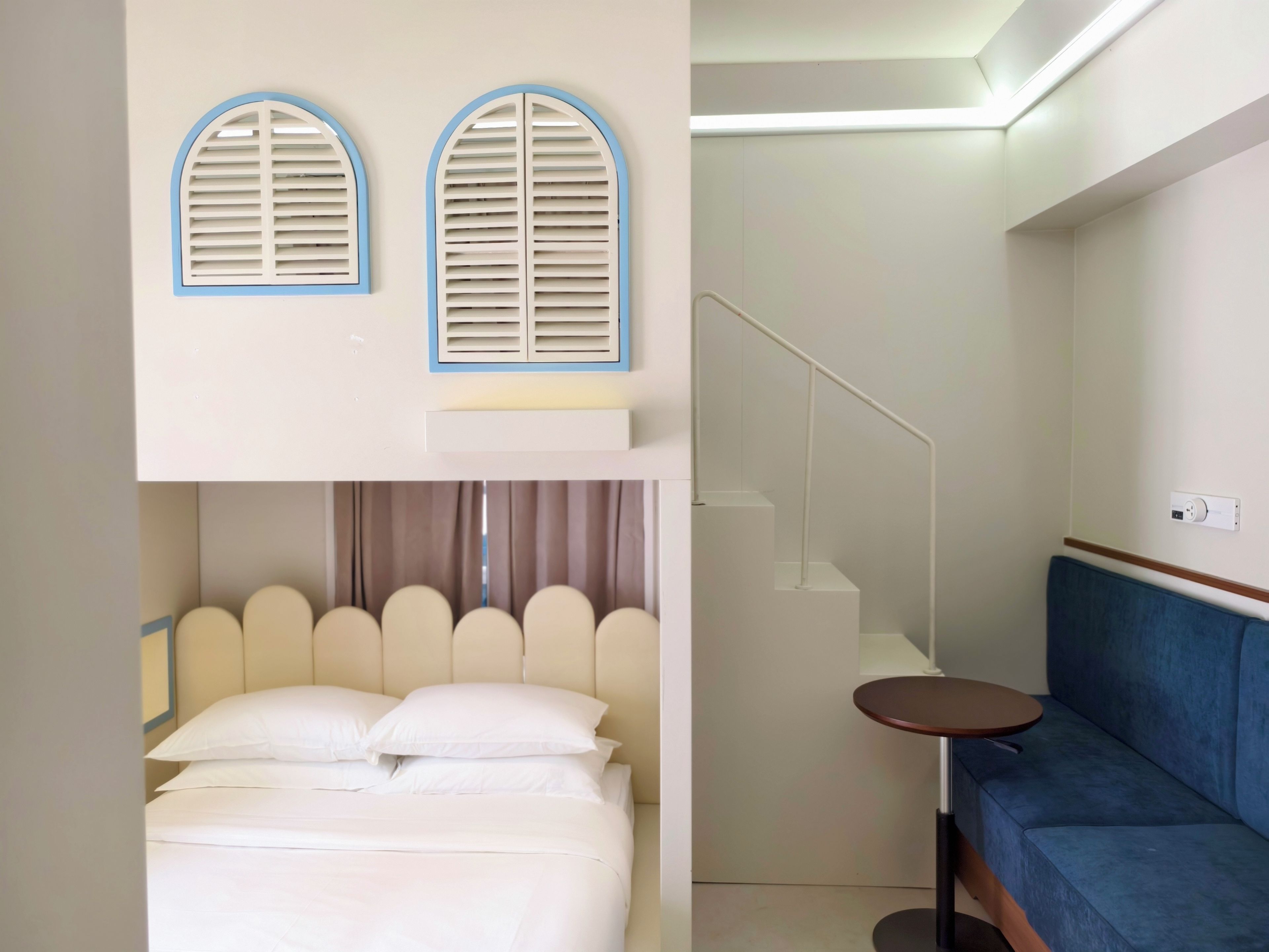 A hotel room with a bed, a blue sofa, a small table, and a staircase.
