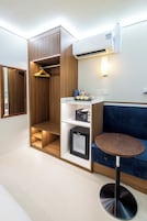 A compact room with a built-in wardrobe, a small kitchenette, a seating area with a round table, and a wall-mounted air conditioning unit.