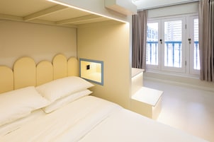 Una habitación de hotel con cama, mesita de noche, lámpara de pared y ventana con cortinas.
