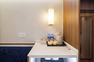 Habitación de hotel con un mostrador blanco, una lámpara de pared, una tetera, una cafetera y una caja de pañuelos.