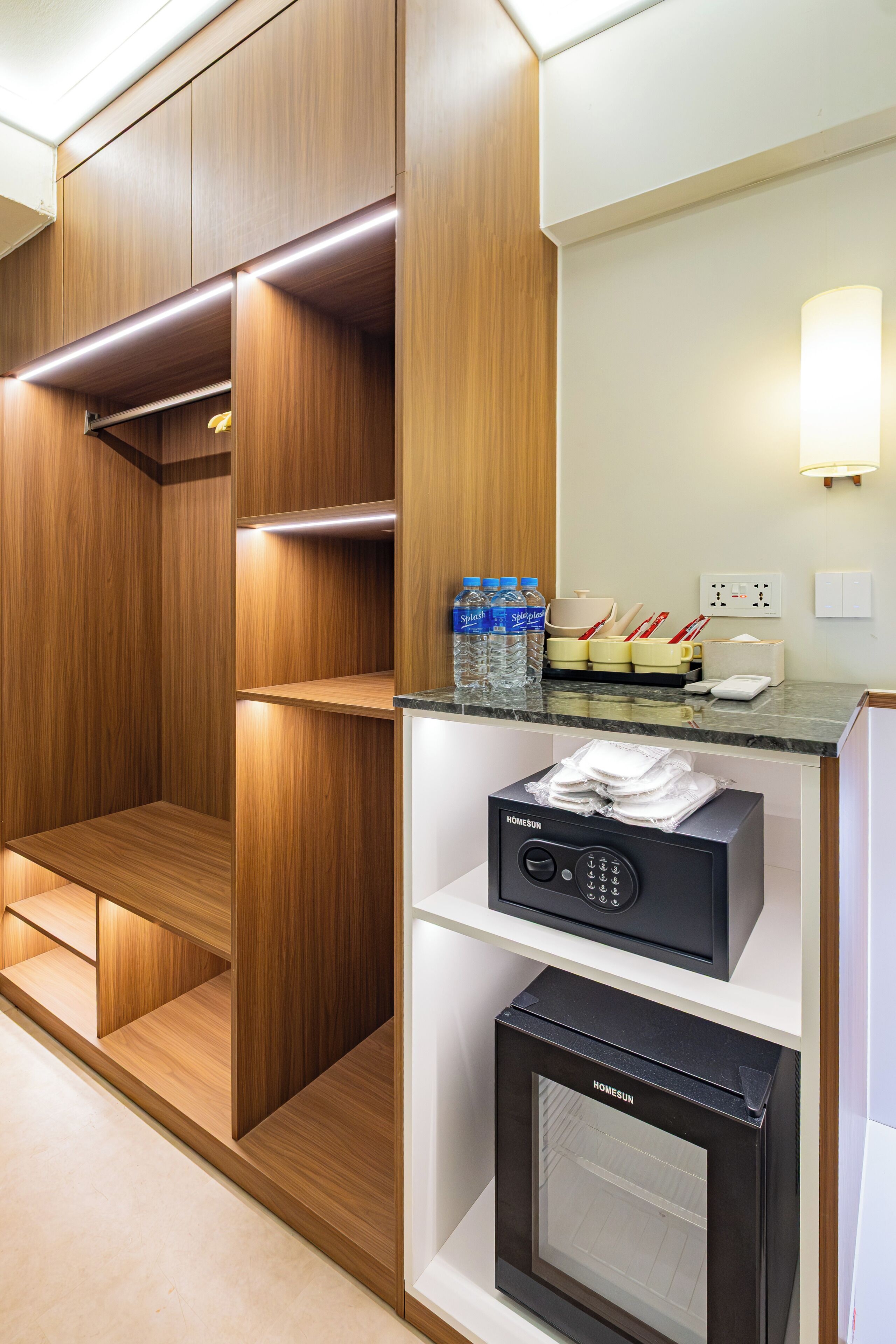 Habitación de hotel con armario empotrado de madera, minibar con botellas de agua, microondas y refrigerador pequeño.