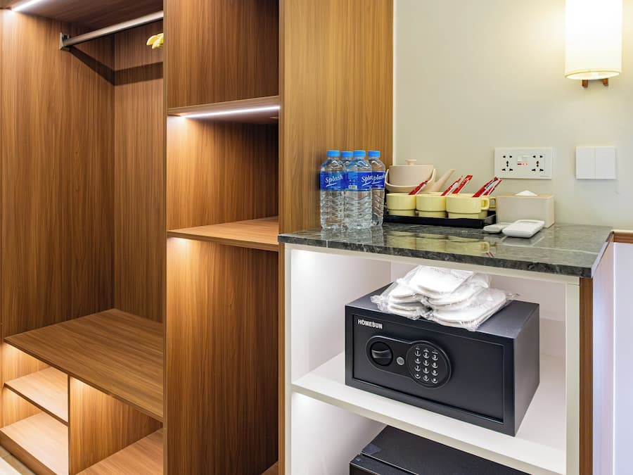 Habitación de hotel con armario empotrado de madera, minibar con botellas de agua, microondas y refrigerador pequeño.