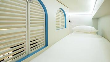 Una habitación con cama, ventana con persianas y una lámpara fijada a la pared.