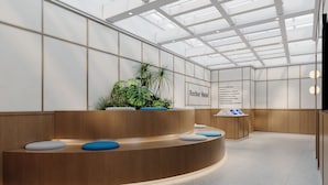 Un área de recepción de hotel con diseño moderno, que incluye un mostrador curvo, zonas de estar y un techo con tragaluces.