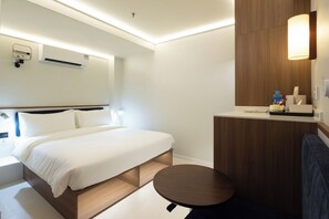 A hotel room with a bed, bedside table, round table, and a mirror with a wooden panel. - Rest Rochor Hotel (Singapore)