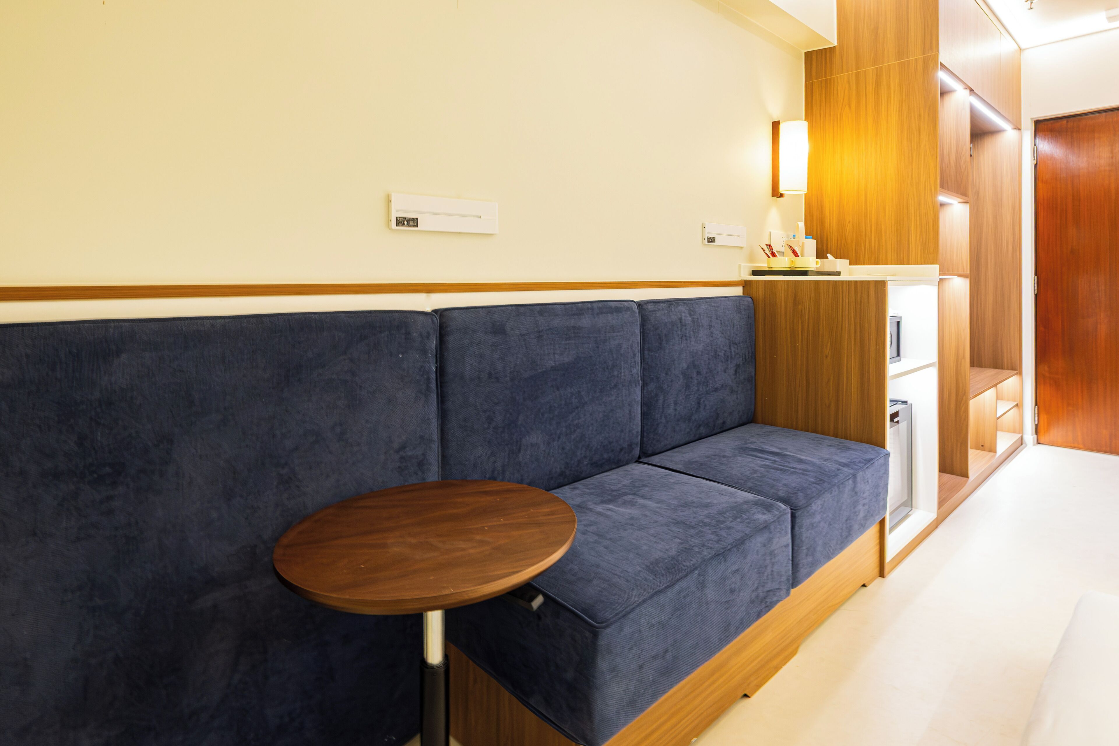 Una habitación de hotel moderna con un sofá azul, una pequeña mesa redonda y un armario de madera.
