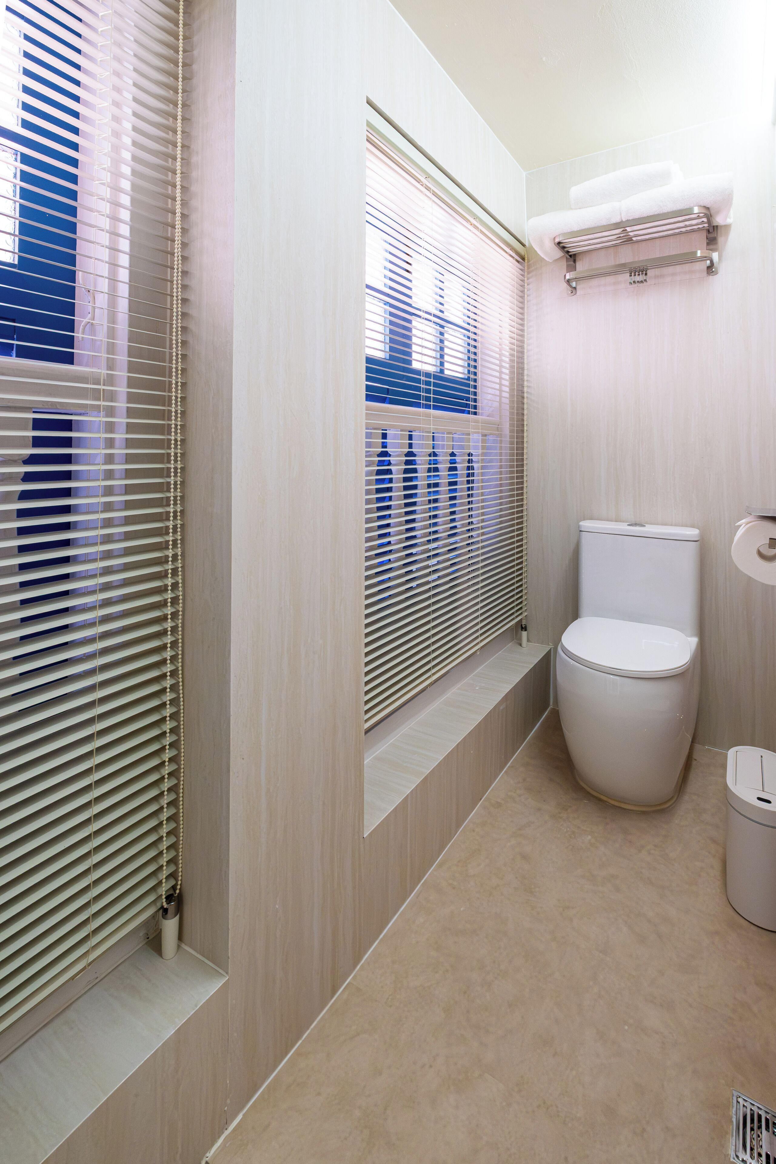Une salle de bain équipée de toilettes, d’un porte-serviettes et d’une fenêtre avec des stores.