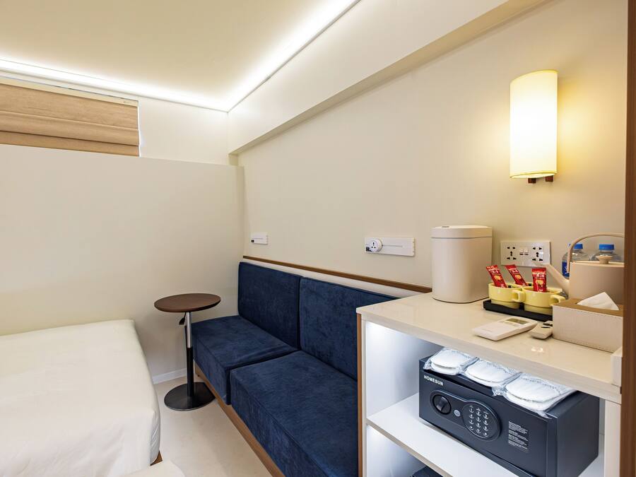 A hotel room with a bed, a blue sofa, a small round table, a minibar, and a wall-mounted lamp.