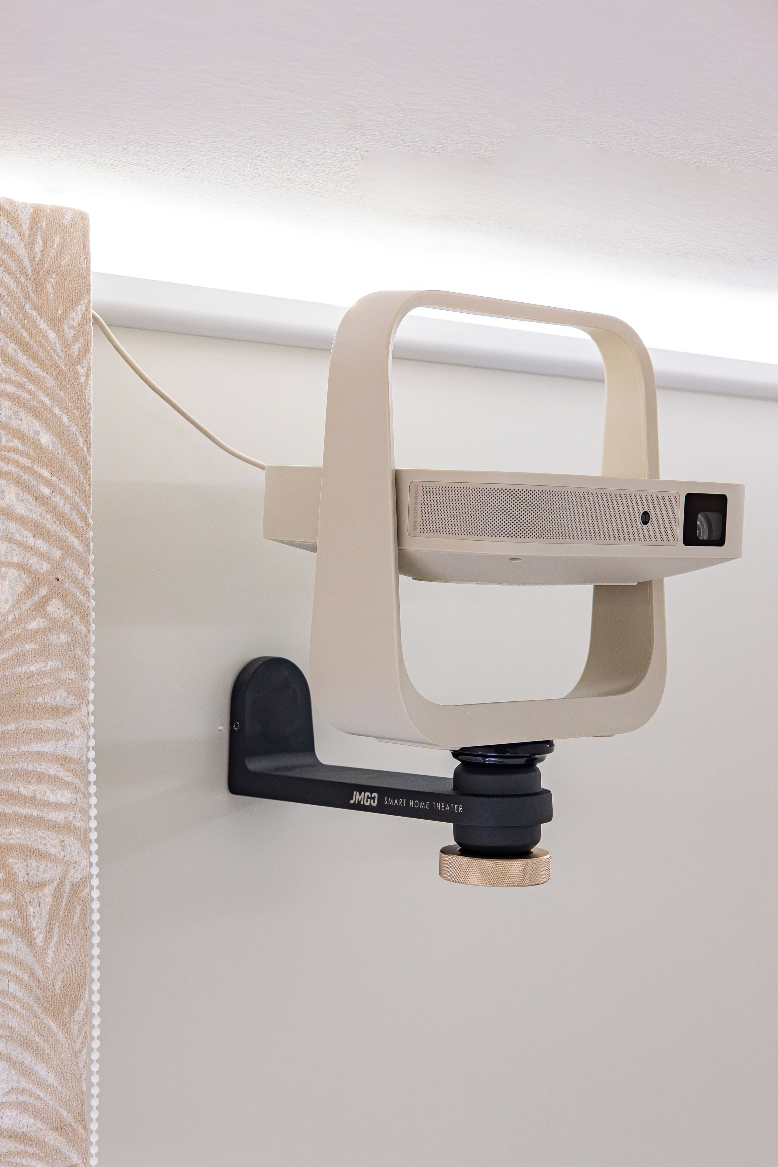 A projector mounted on a wall with a remote control and a power cable.