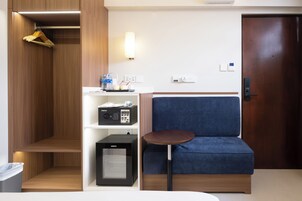 A hotel room with a wardrobe, a minibar, a seating area, and a door.
