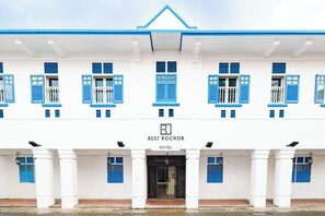 A hotel facade with a symmetrical design, featuring a central entrance, multiple windows with blue shutters, and a sign indicating it is the Rest Rochor Hotel.
