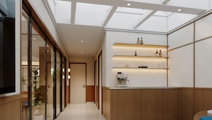 Un interior moderno con puerta de vidrio de entrada, una zona de cocina con cafetera y un techo con tragaluces.