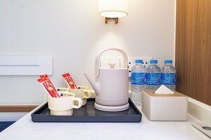 A hotel room with a tray table, a white kettle, cups with Nescafé packets, a tissue box, and bottled water.