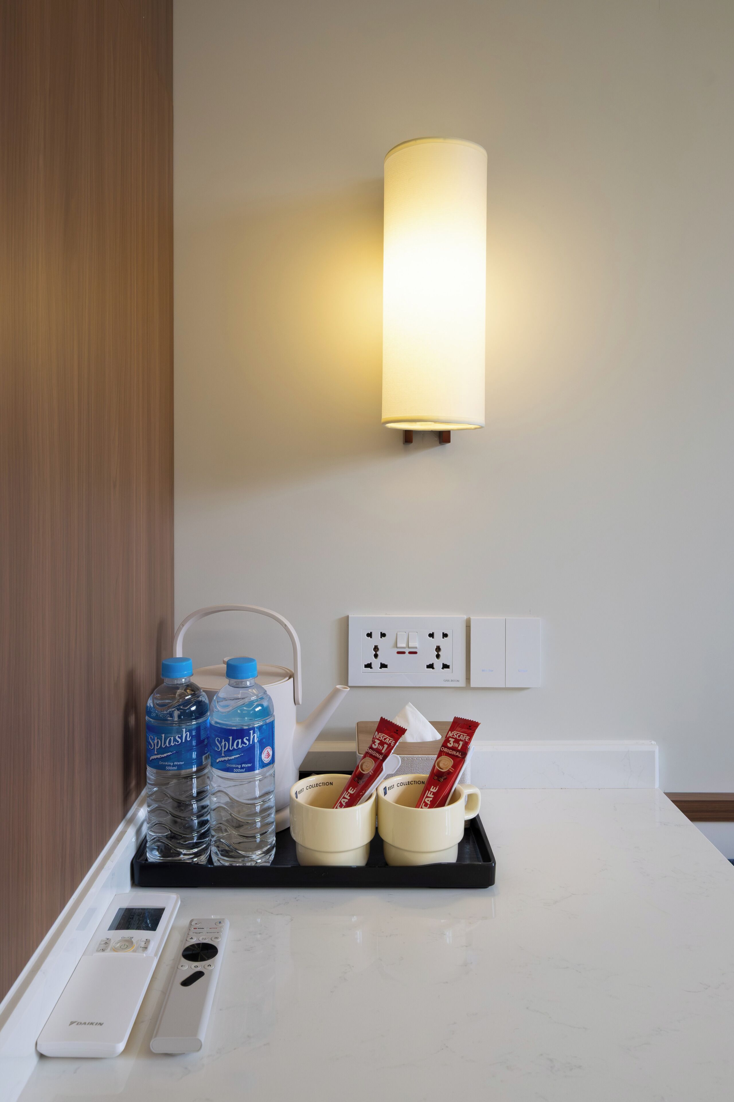 Ein Hotelzimmer mit Nachttisch, einer Wasserflasche, einer Tasse und einer Fernbedienung.
