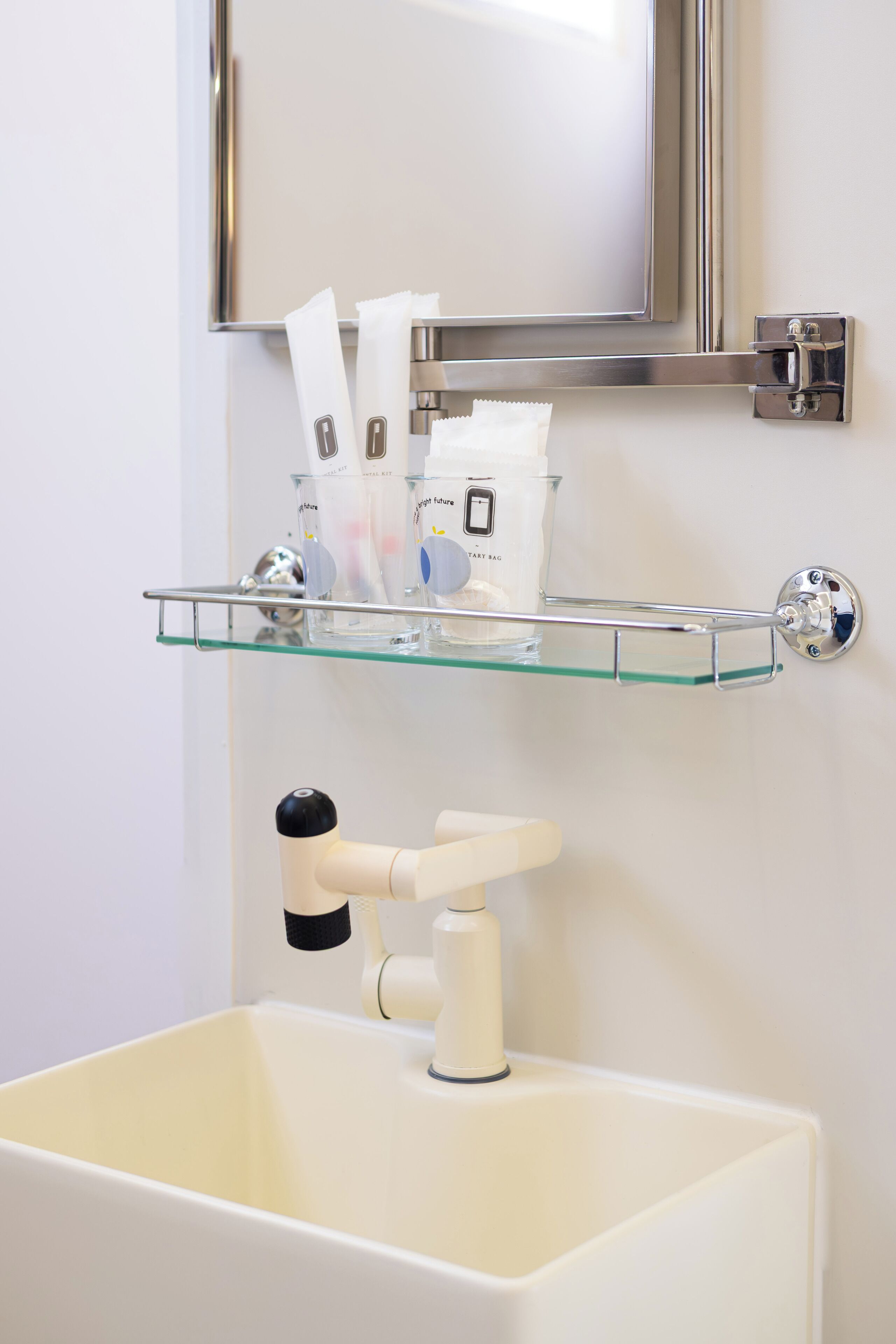 A bathroom with a glass shelf holding toiletries, a white sink, and a mirror above.