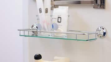 A bathroom with a glass shelf holding toiletries, a white sink, and a mirror above.