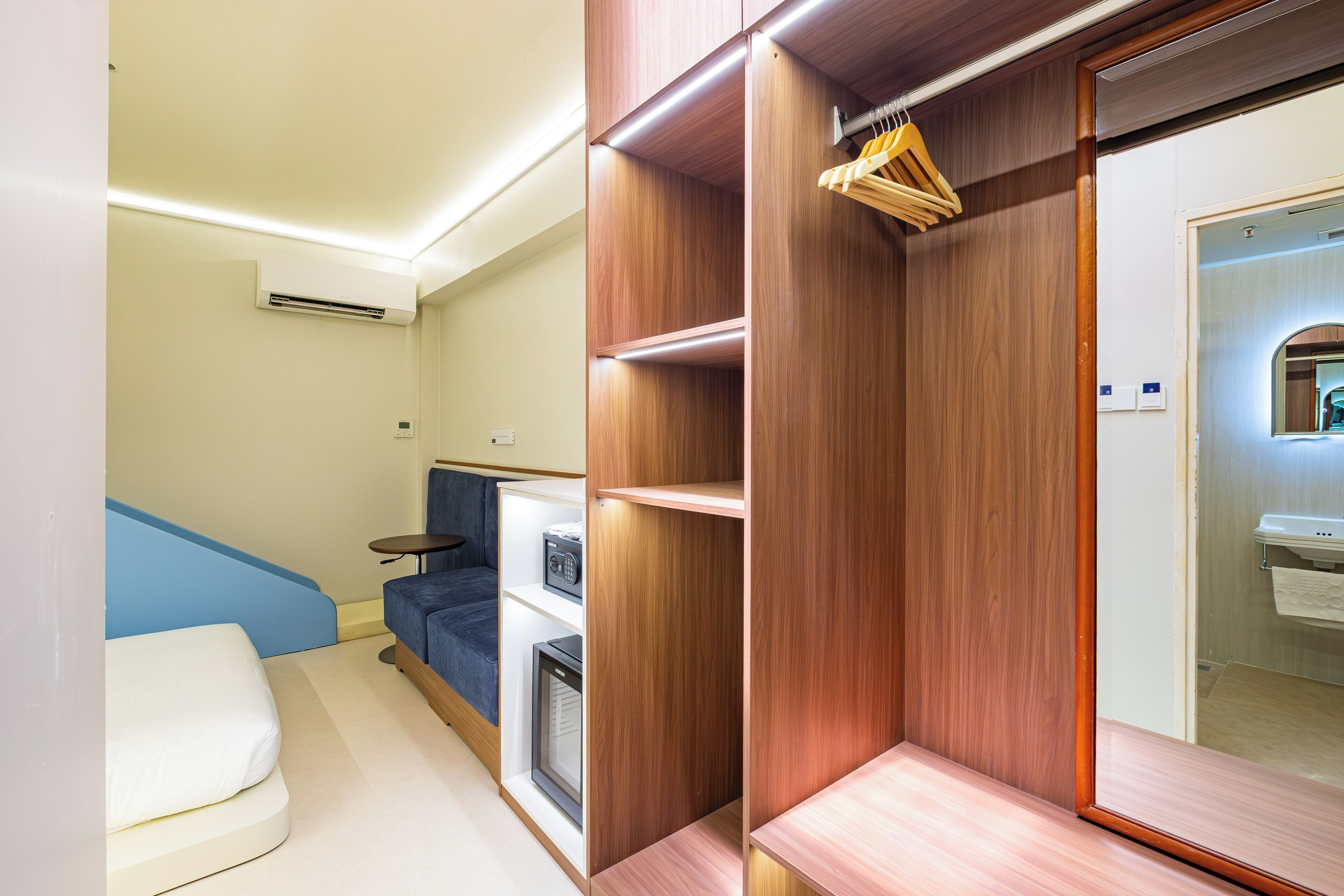 Una habitación moderna con armario empotrado, una zona de estar con sofá azul y una pequeña mesa.