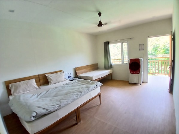 A single-bed room with a wooden headboard, a bedside table with a lamp, a window with curtains, and a red heater.