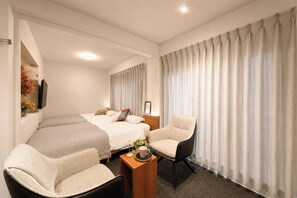 Una habitación de hotel con una cama, dos sillones, una mesita con una taza y cortinas.