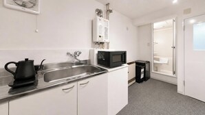 Una kitchenette compacta con pileta de acero inoxidable, hervidor de agua, microondas y un basurero pequeño.