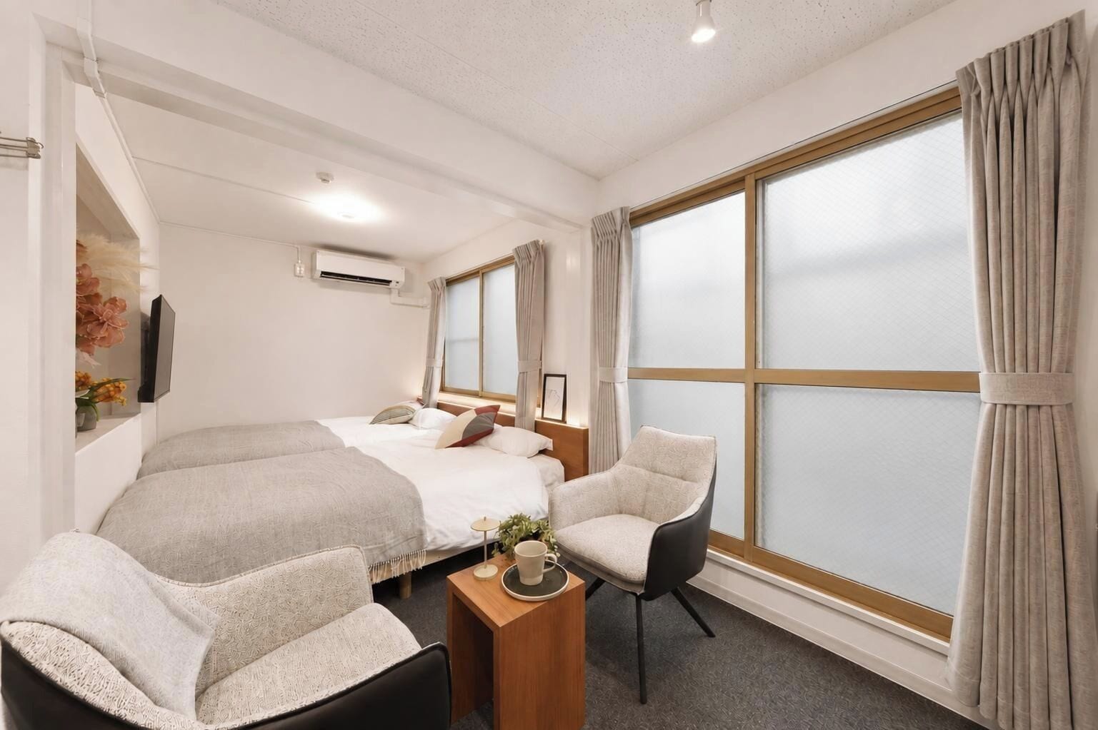 A hotel room with a bed, two chairs, a small table, and a large window with curtains.