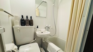 Un baño pequeño con inodoro, lavamanos y bañera. Hay tres botellas de productos de cuidado corporal Hajimari sobre el tanque del inodoro.
