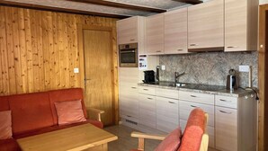 A compact kitchen with wooden cabinets, a built-in oven, and a countertop with a coffee maker. - Chalet Allegra Appartement/Fewo, Dusche, WC 4-Bettwohnung Erdgeschoss by Interhome (Rosswald)