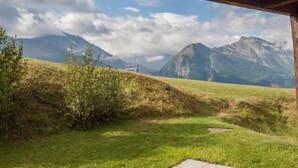 A grassy field with a wooden structure, a mountain range in the background, and a clear sky. - Chalet Allegra Appartement/Fewo, Dusche, WC 4-Bettwohnung Erdgeschoss by Interhome (Rosswald)