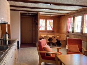 Interior acolhedor de uma cabana, com cozinha, área de jantar e espaço para sentar.
