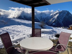 Zona de estar exterior cubierta de nieve, con una mesa y sillas, con vistas a un paisaje montañoso.