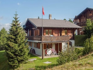 A two-story wooden chalet with a balcony, surrounded by greenery. - Chalet Allegra Appartement/Fewo, Dusche, WC 4-Bettwohnung Erdgeschoss by Interhome (Rosswald)