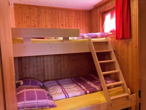 A bunk bed with a wooden ladder, a window with red curtains, and a wooden wall. - Chalet Allegra Appartement/Fewo, Dusche, WC 4-Bettwohnung Erdgeschoss by Interhome (Rosswald)