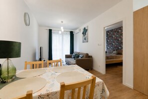 A dining area with a table, chairs, and a lamp. There is a sofa and a bed in the background. - Apartamenty Sun & Snow Polanica Park (Polanica-Zdrój)