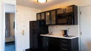 Eine kleine Küche mit dunklen Schränken, einem schwarzen Kühlschrank, einer Mikrowelle und einer Kaffeemaschine.