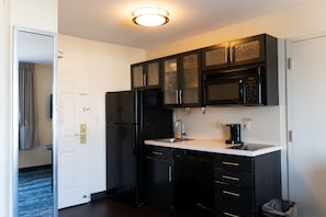 Cocina compacta con muebles oscuros, un refrigerador negro, microondas y cafetera.