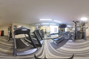 Un gimnasio con cintas de correr, pesas y un espejo grande.