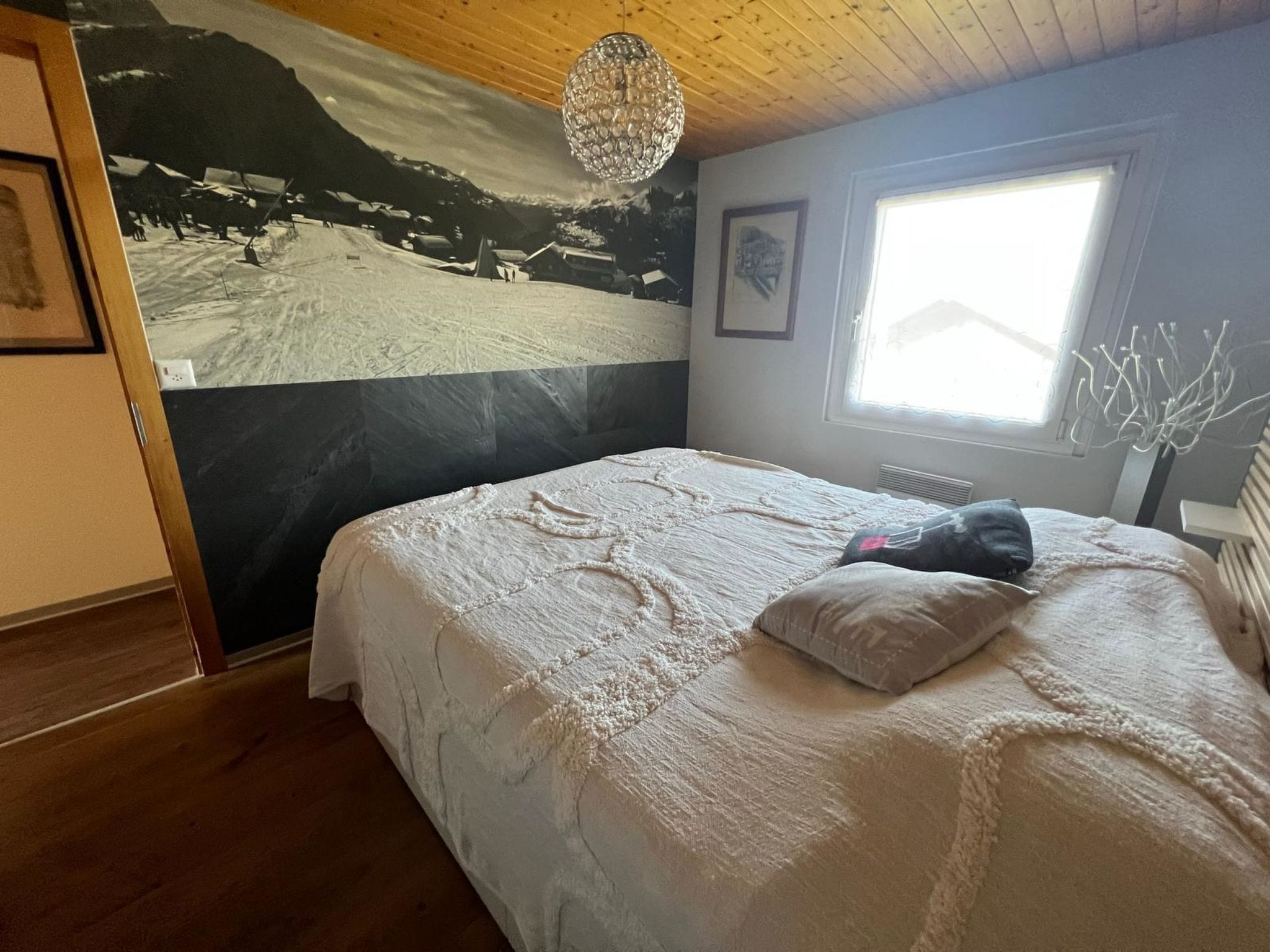 Un dormitorio con una cama grande, una ventana con vistas, una araña y un mural en la pared.