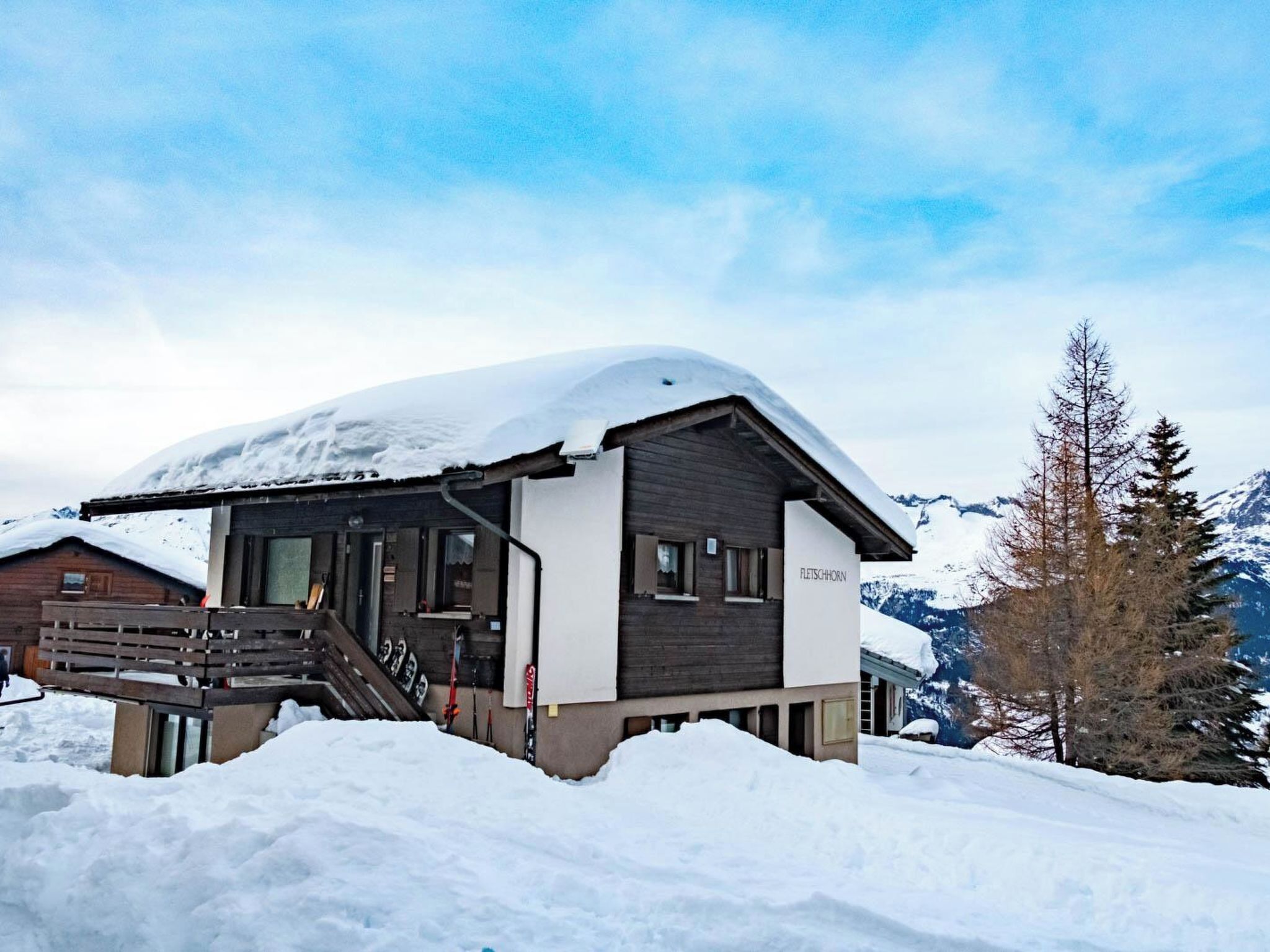 Ein mit Schnee bedecktes Chalet mit einer Holztreppe zum Eingang, einer Seilbahn und einem Berg im Hintergrund.