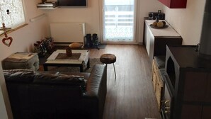 Ein Wohnzimmer mit einer Couch, einem Couchtisch, einem Fernseher und einem Fenster mit Vorhängen.