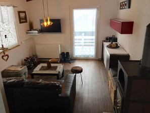 Ein Wohnzimmer mit einer Couch, einem Couchtisch, einem Fernseher und einem Fenster mit Vorhängen.