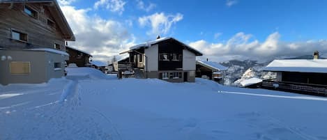 A snow-covered village with traditional wooden houses, a clear sky, and a mountain in the background.