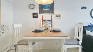Ein Essbereich mit einem Holztisch, weißen Stühlen, einem gerahmten Bild, einer Uhr und einer Wandleuchte.