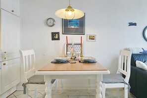 A dining area with a wooden table, white chairs, a framed picture, a clock, and a wall-mounted light fixture. - Seebrücke Apartment 11 (Scharbeutz)