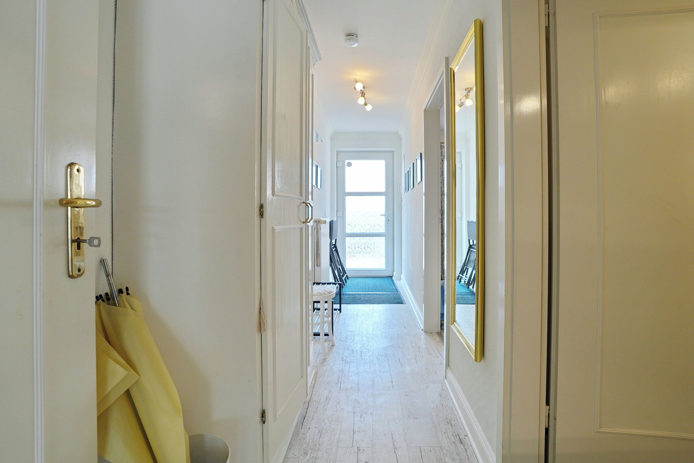A hallway with white walls, a wooden floor, and a door with a golden handle.