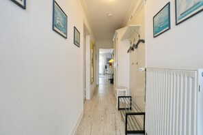 A hallway with framed artwork on the walls, a radiator, and a small table with a chair. - Seebrücke Apartment 11 (Scharbeutz)