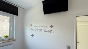 Una habitación con televisión montada, una ventana con vista al exterior y una pared con una cita motivacional.