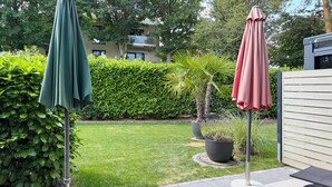 Un patio con dos sombrillas, un banco y un césped bien cuidado.