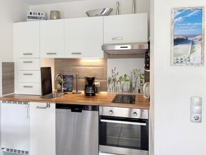 A modern kitchen with white cabinetry, a coffee maker, and a Siemens dishwasher. - "Sandkorn 1" Apartment (Scharbeutz)