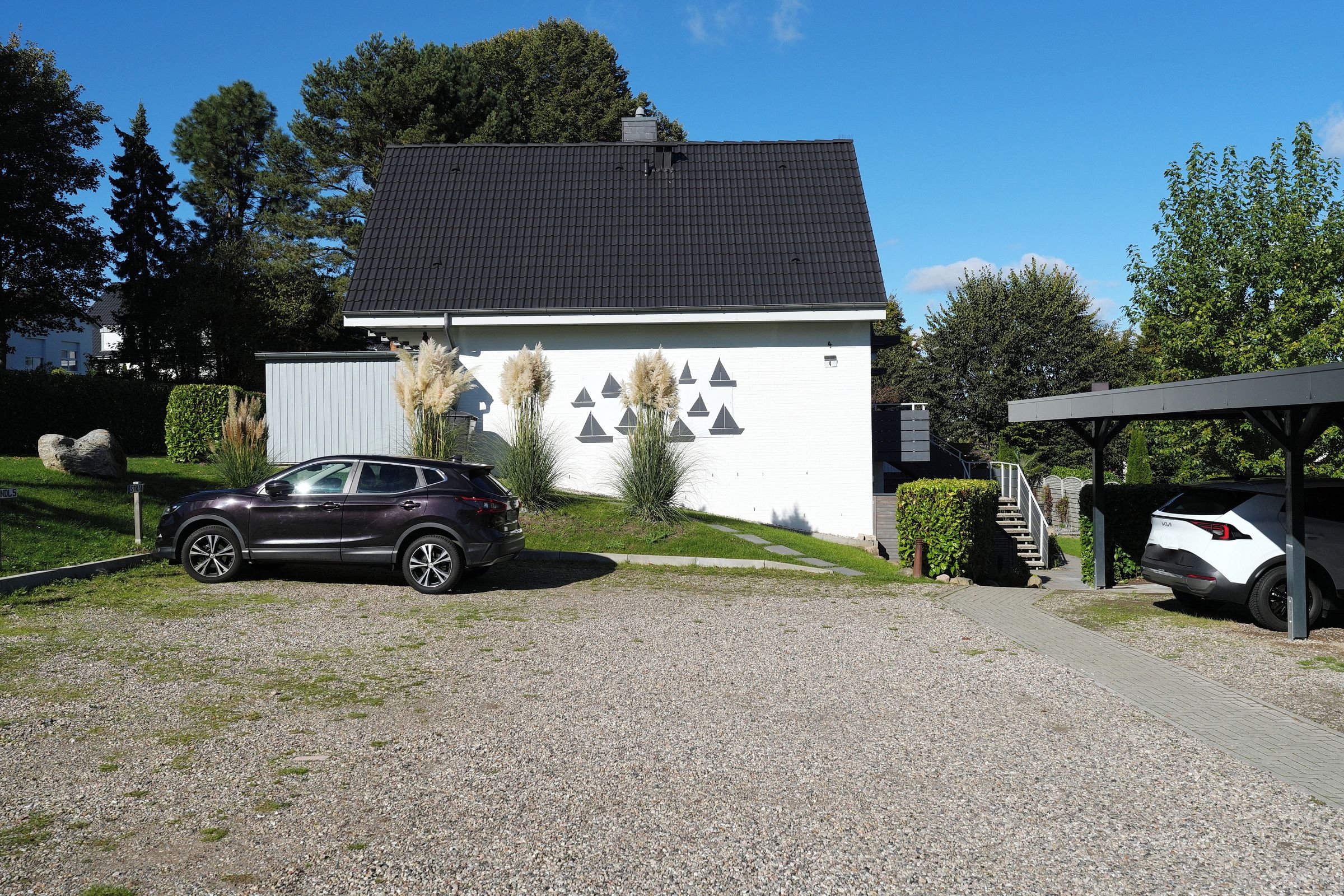 A modern house with a gravel driveway, parked cars, and a covered carport.