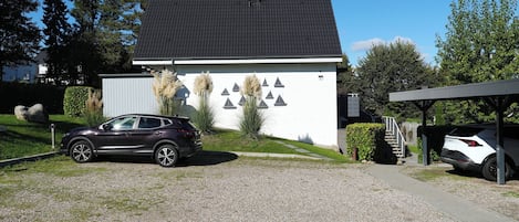 A modern house with a gravel driveway, parked cars, and a covered carport.